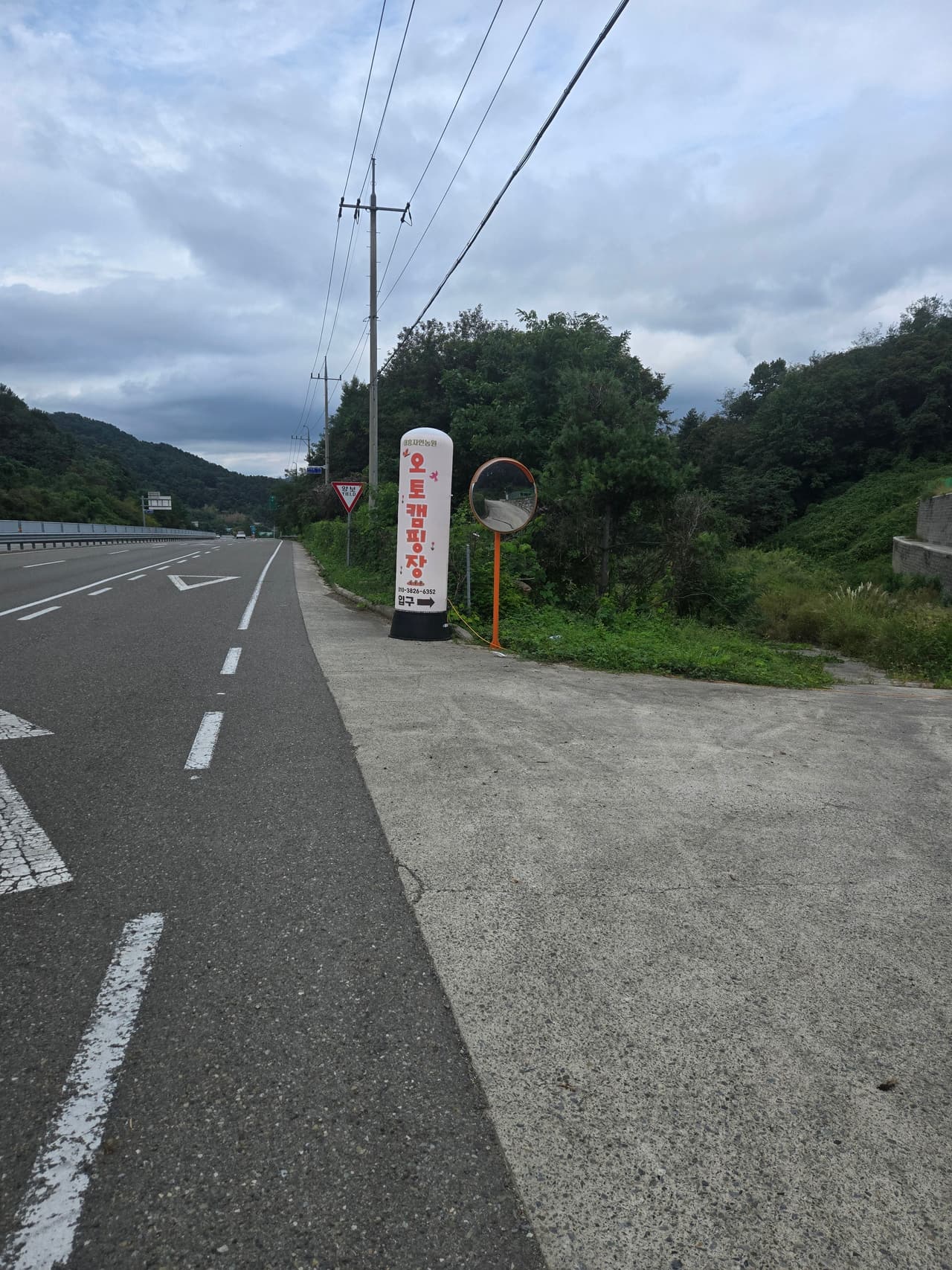 국도 가장자리에 선 캠핑장 흰 입간판과 반사경, 그 옆으로 꺾여 들어가는 시멘트 진입로