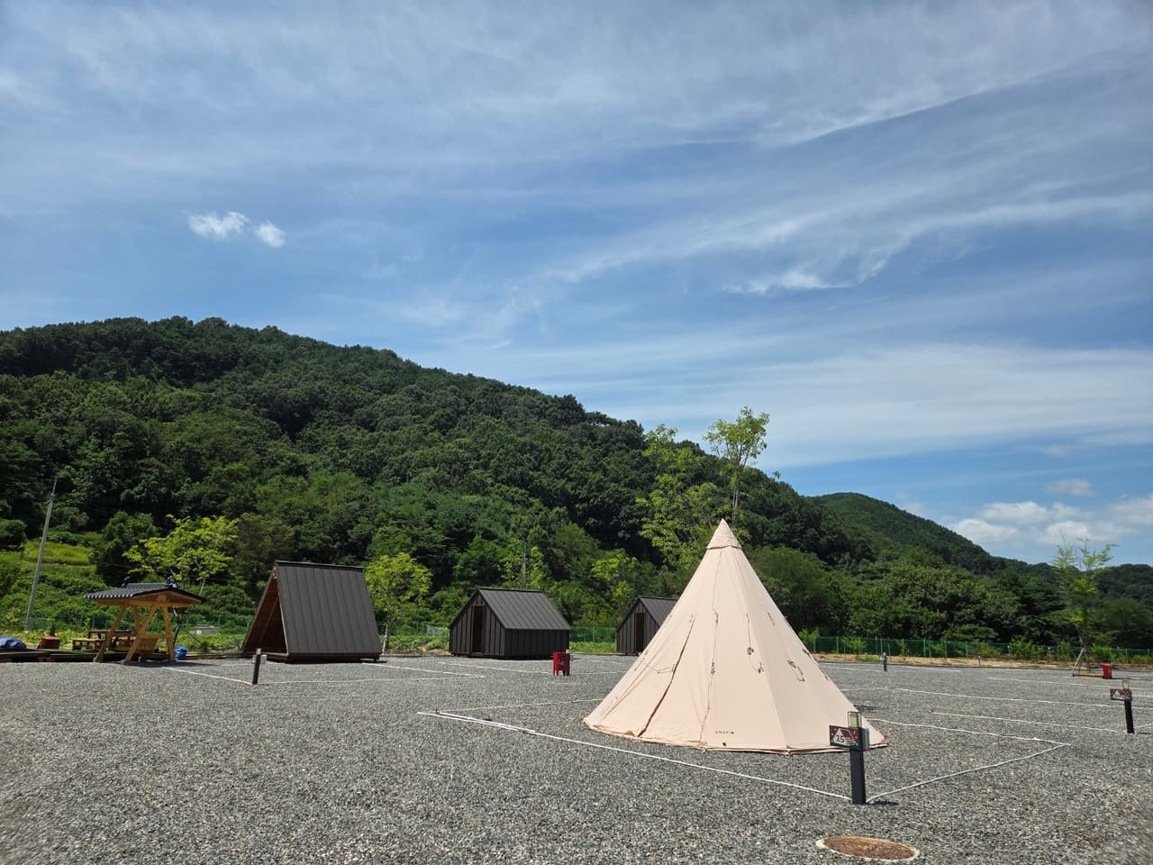 山の稜線を背に、キャビンと円錐形のテントが並ぶキャンプ場